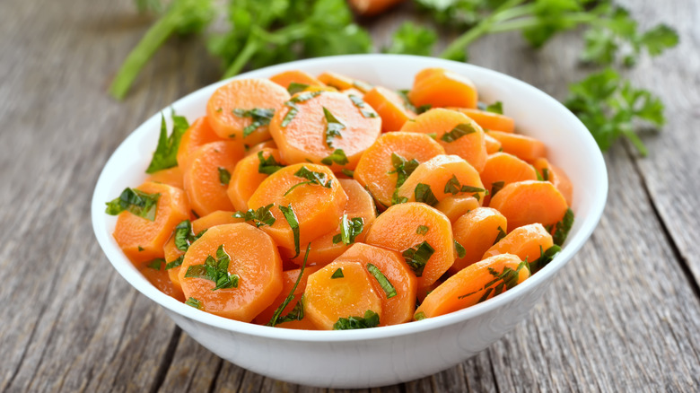 Steamed carrots garnished with herbs in white bowl