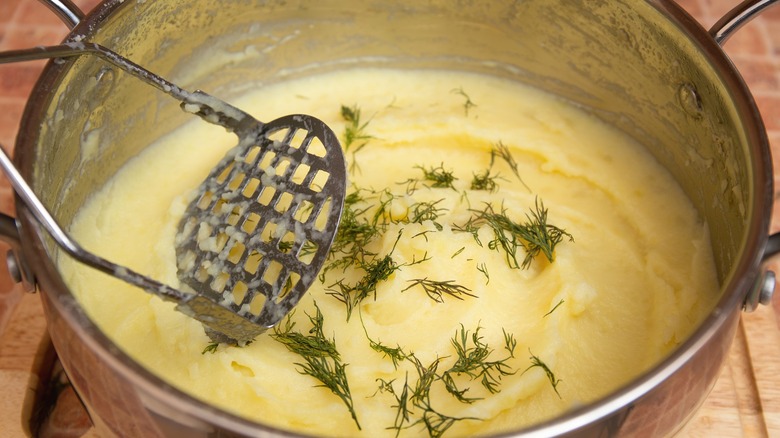 Person making mashed potatoes with masher in stainless steel bowl