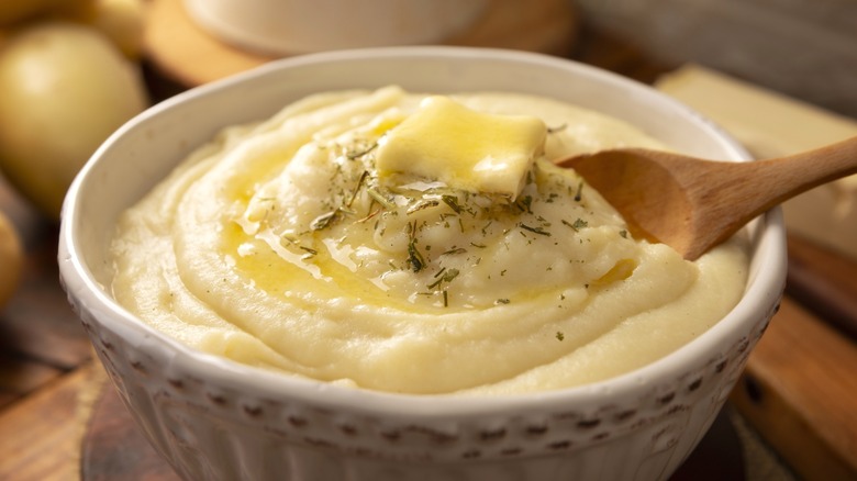 Mashed potatoes with butter in white bowl with wooden spoon