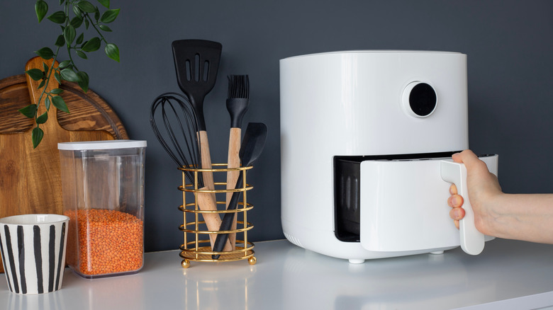 Hand opening white air fryer on kitchen counter