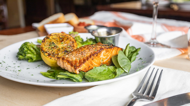 A grilled salmon on a bed of spinach alongside a grilled lemon on a white plate.