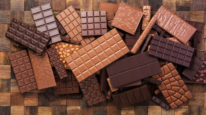 Several assorted, full-sized chocolate bars laid out in a pile on wooden surface