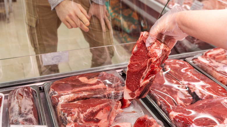 A butcher shows a cut of beef to a customer