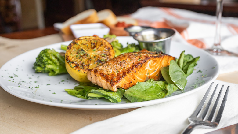 A grilled salmon on a bed of spinach alongside a grilled lemon on a white plate.