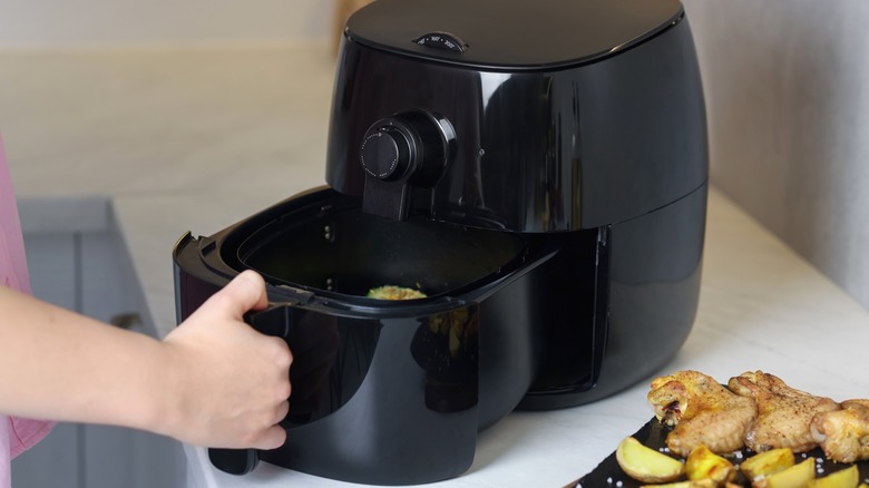 Person opening black air fryer on white kitchen countertop