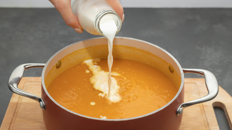 Adding cream to a pot of pureed pumpkin soup
