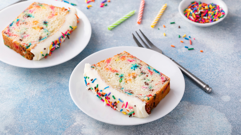 Sliced rainbow sprinkle loaf cake on plates with sprinkles and birthday candles
