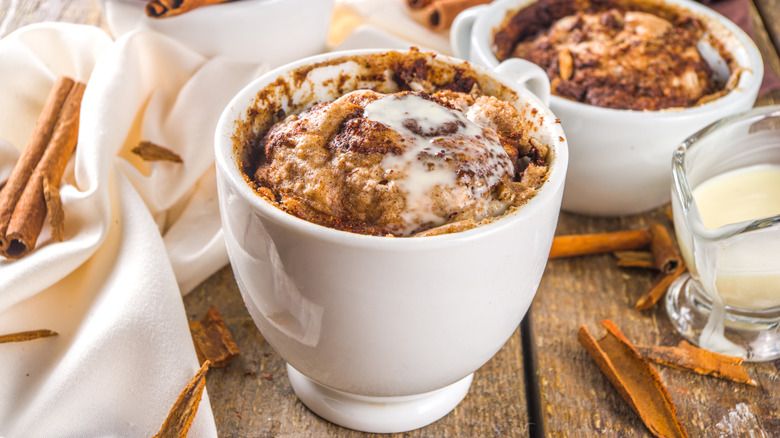 a cinnamon roll in a mug garnished with icing and surrounded by ingredients