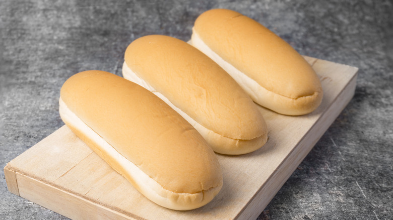 Three hot dog buns on a wooden chopping board