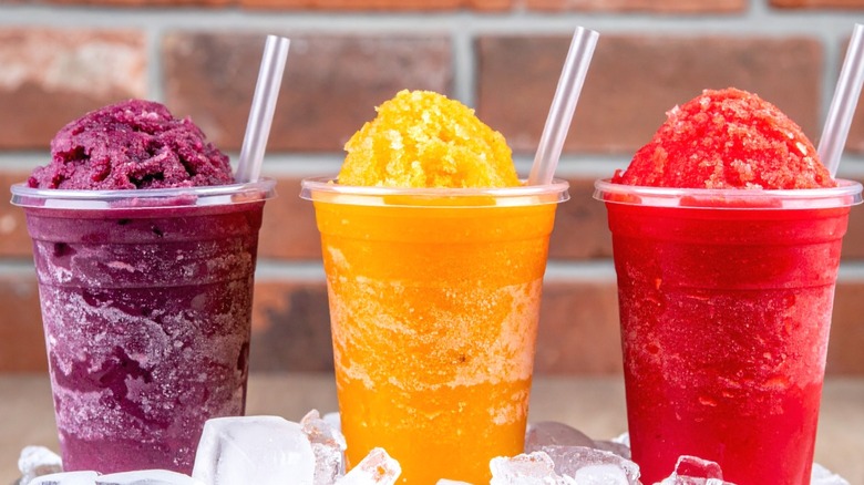 Three slushies (purple, yellow, and red) in plastic cups with plastic straws.