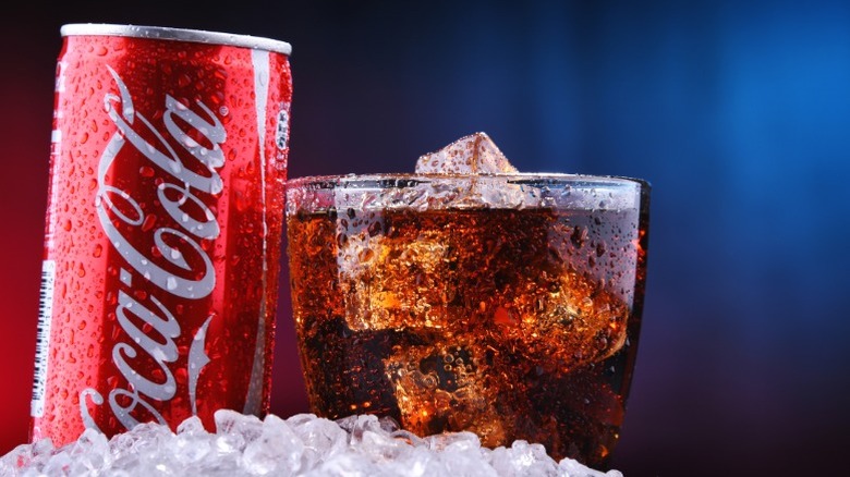 A glass and can of Coca-Cola in a mound of ice.