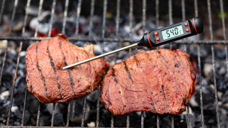 A digital meat thermometer sticks out of a steak on a grill