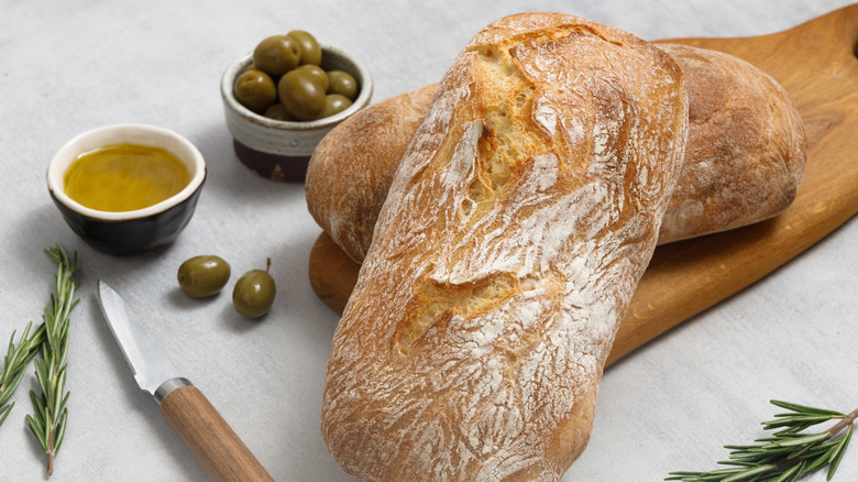 Wooden paddle with sourdough, rosemary, and olive oil on stone surface.