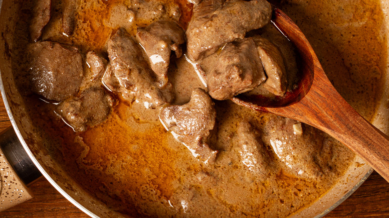 Beef stroganoff in a metal pot and a wooden spoon.