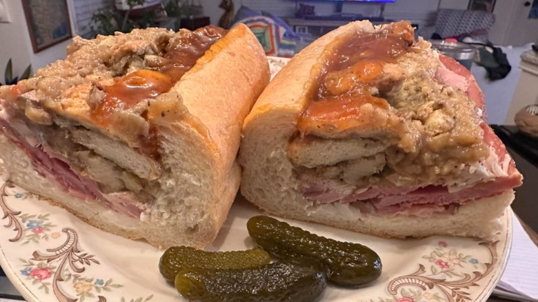 Turkey, ham, stuffing, and gravy sandwich on a patterned plate with three gherkins