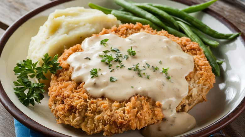 Chicken-fried steak with white gravy, mashed potatoes, and green beans.