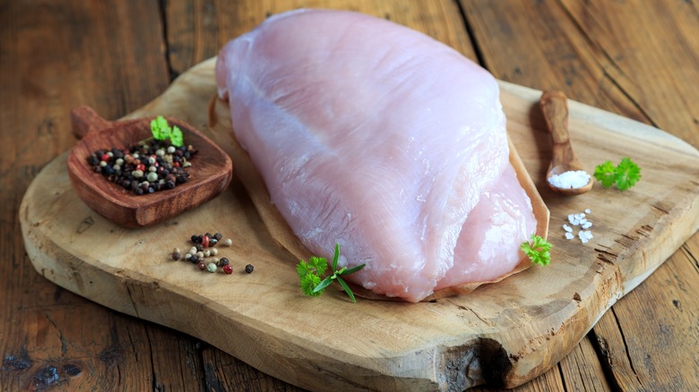 Raw turkey breast on board with peppercorns and salt