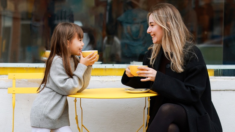 Child with mother outside cafe drinking coffee