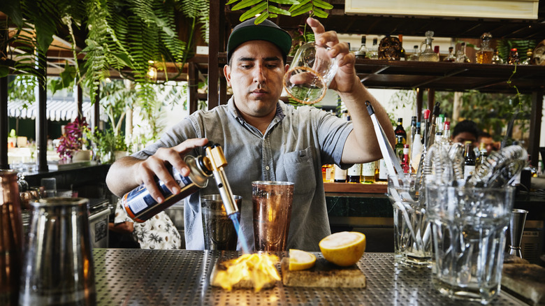 A craft bartender torching some fruit for a drink