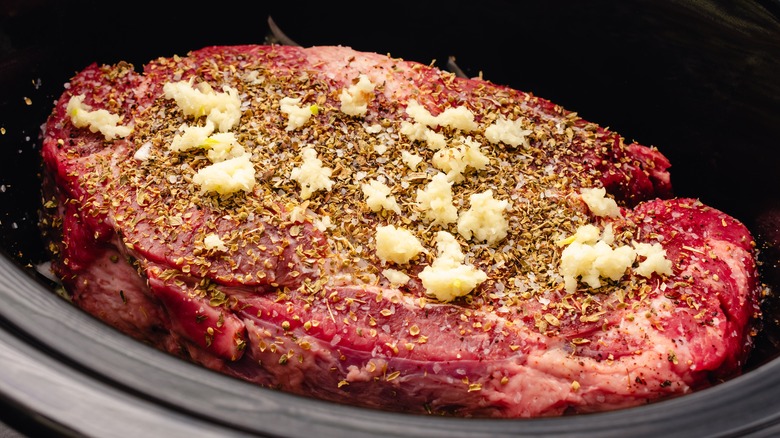 A cut of steak with seasonings sitting in a slow cooker