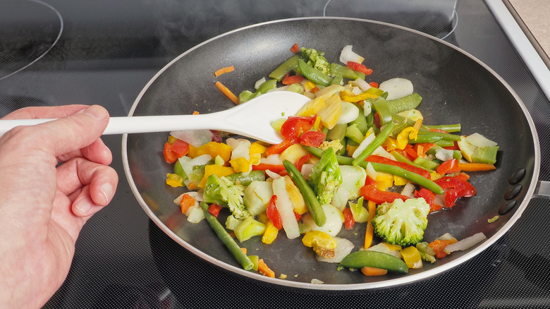 Someone stir frying vegetables in a nonstick pan with a white spoon