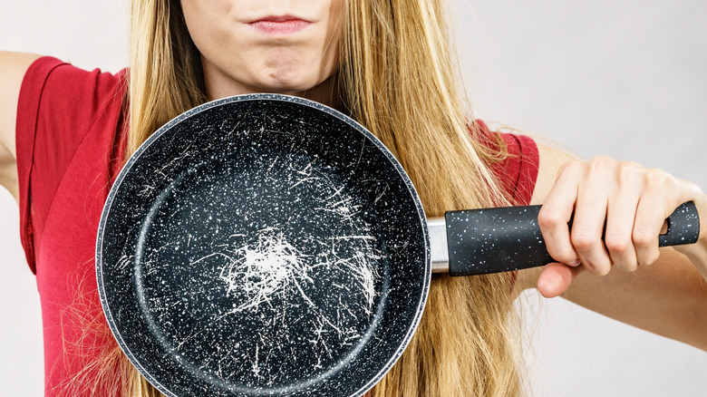 An angry woman displaying a very scratched nonstick pan