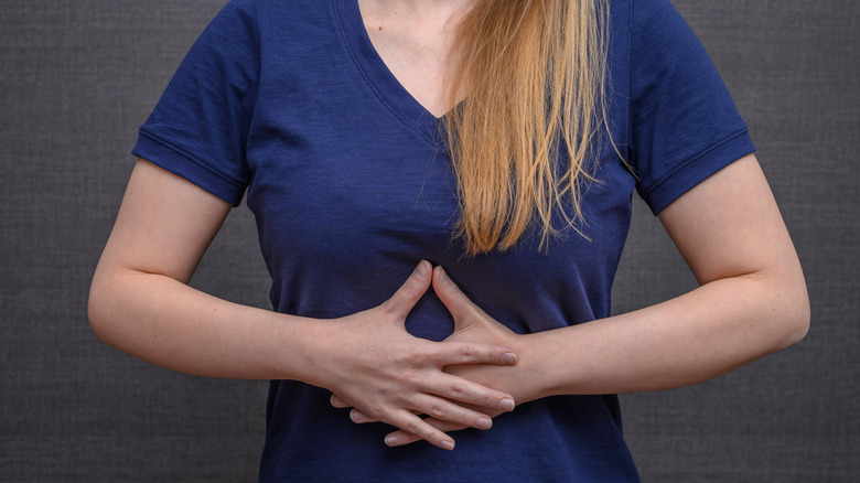 A woman in a blue V-neck t shirt clasps her hands over her stomach