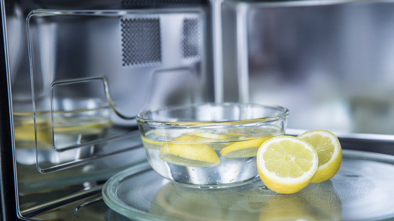 A bowl of water with lemon slices and two lemon halves rest in a microwave