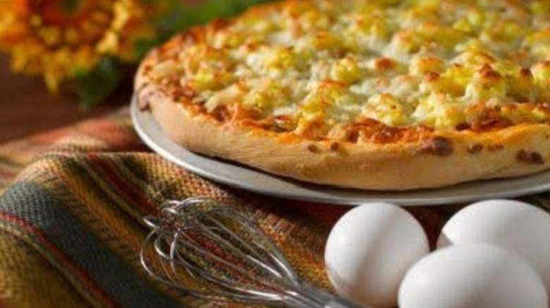 A breakfast pizza styled with eggs and a metal whisk
