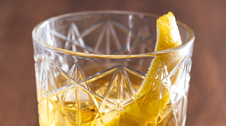A rusty nail cocktail is garnished with citrus peel