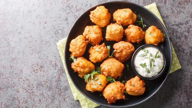 Black plate of hushpuppies and dip with herbs