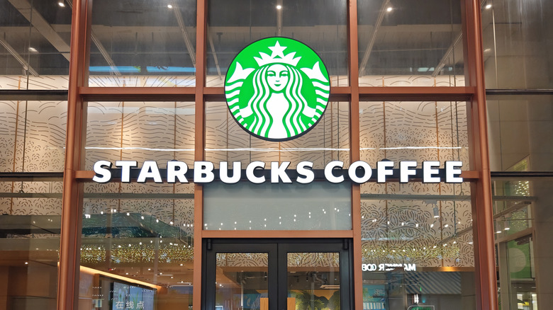 A Starbucks Coffee sign on the exterior of a Starbucks location with large windows.