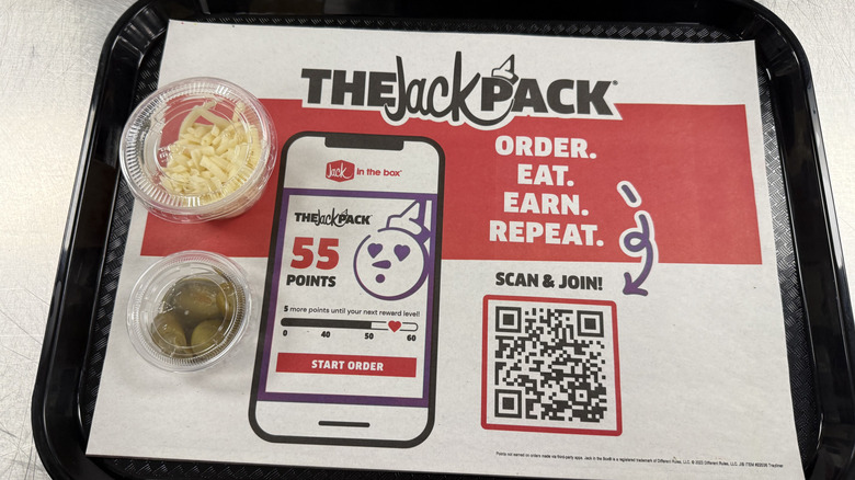a menu with a Jack in the Box paper liner, and two plastic takeout ramekins of shredded cheese and pickled jalapeños