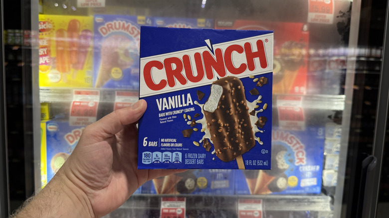 Hand holding a box of Crunch Ice Cream Bars in front of a freezer