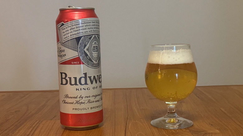 A tall can of Budweiser next to a full goblet of beer.