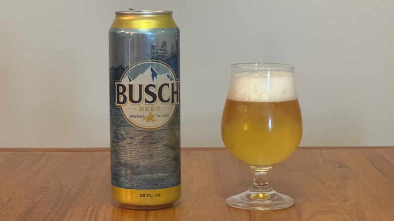 A tall can of Busch next to a full beer glass with a frothy head.