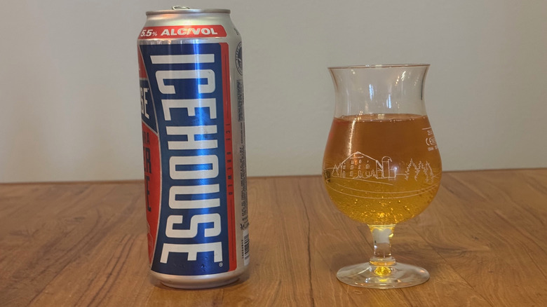 A tall can of icehouse next to a full beer glass without any head on the beer.