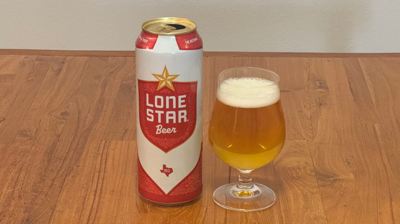 A tall red and white can of Lone Star next to a full, curved beer glass.