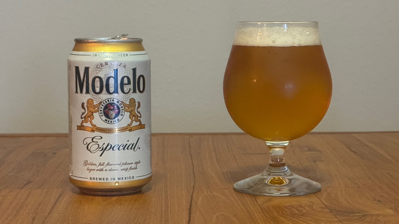 A can of Modelo next to a full beer goblet with a thin layer of froth at the top.