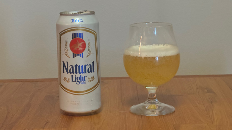 A 16-ounce can of Natural Light beside a stemmed glass filled with pale yellow beer and a thin layer of foam.
