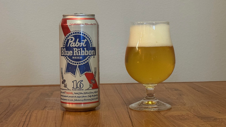 A can of Pabst Blue Ribbon next to a full beer glass with a head of foam.