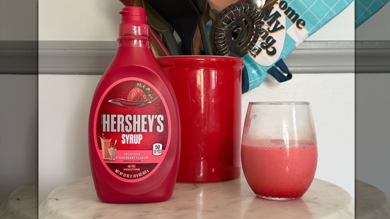 A bottle of Hershey's strawberry syrup next to a glass of strawberry milk