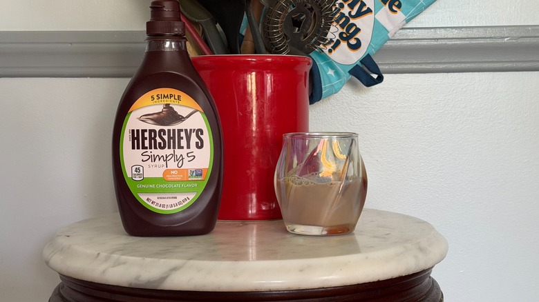 A bottle of Hershey's Simply 5 chocolate syrup next to a small glass of chocolate milk