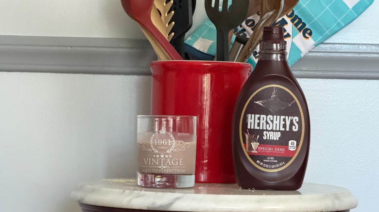 A bottle of Hershey's special dark chocolate syrup next to a small glass of chocolate milk