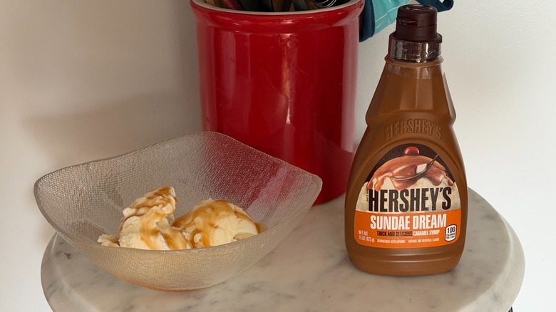 A bottle of Hershey's Dream Sundae caramel syrup next to a bowl of vanilla ice cream with caramel syrup on it