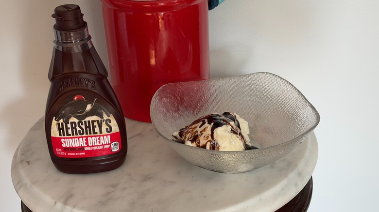 A bottle of Hershey's Sundae Dream double chocolate syrup next a bowl of vanilla ice cream with chocolate syrup on it