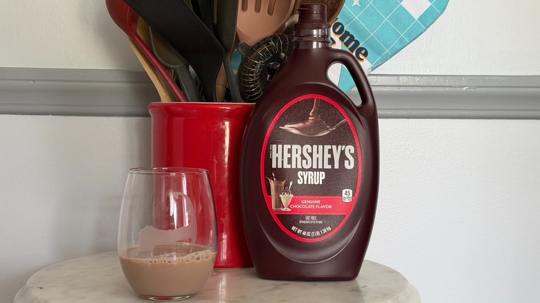 A bottle of Hershey's chocolate syrup next to a small glass of chocolate milk