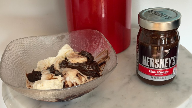 A jar of Hershey's hot fudge next to bowl with vanilla ice cream and hot fudge in it