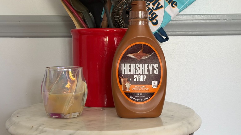 A bottle of Hershey's caramel syrup next to a glass of caramel milk