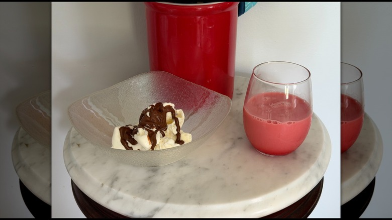 A bowl of vanilla ice cream with chocolate syrup on it next to a glass of strawberry milk